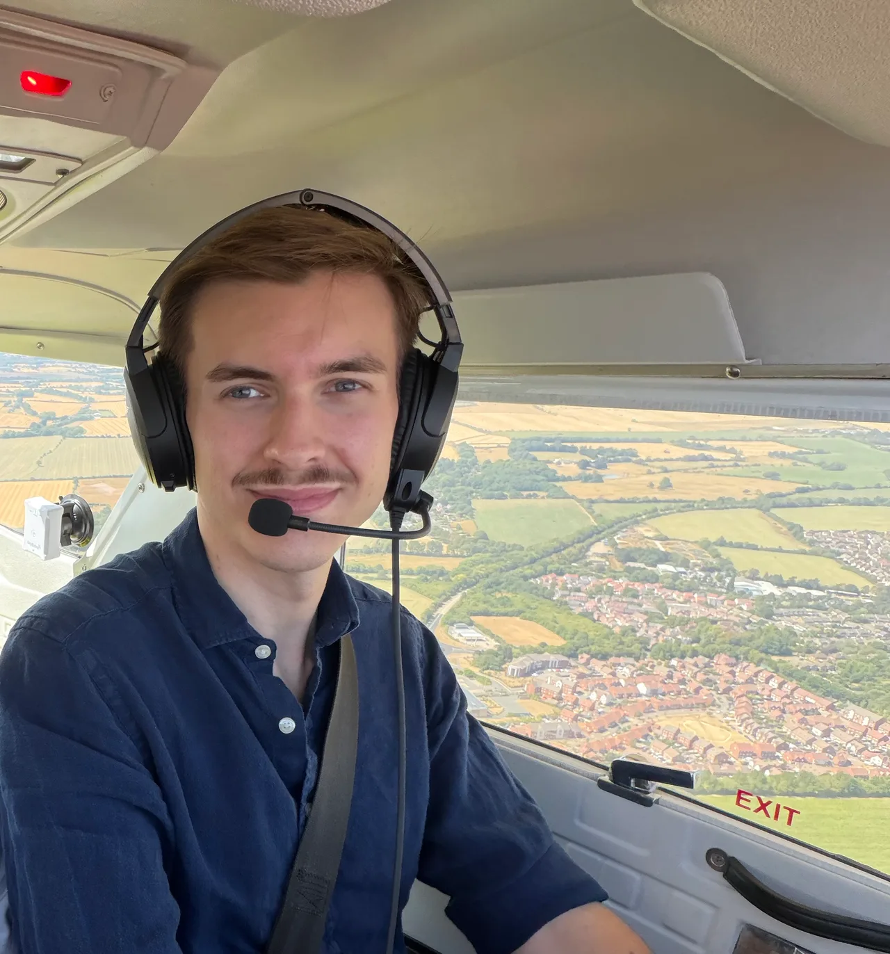 George wearing a headset in a light aircraft, with countryside below